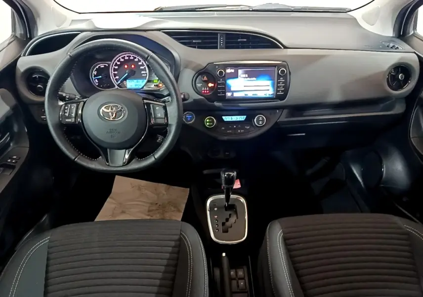 Vue intérieure frontale du tableau de bord et volant cuir noir de la Toyota Yaris hybride 2019 avec écran tactile central.