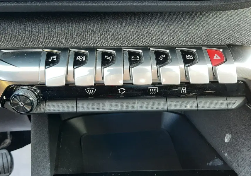 Gros plan sur la rangée de boutons chromés et noirs de la console centrale du Peugeot 3008 noir, avec commandes multimédia et climatisation.
