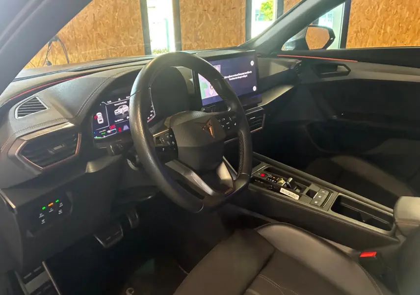 Vue intérieure côté conducteur de la CUPRA Formentor 1.4 E-HYBRID 2024, tableau de bord et volant noirs avec touches modernes.