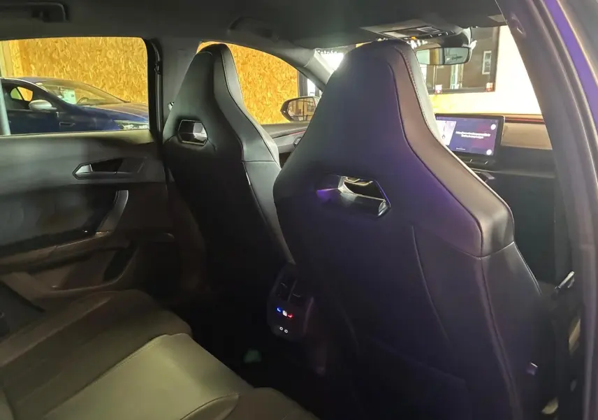 Vue intérieure arrière droite du CUPRA Formentor 1.4 E-HYBRID 2024 avec sièges sport noirs et écran tactile avant visible.