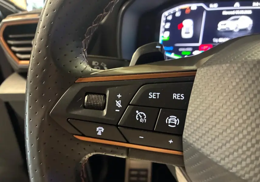 Gros plan sur les commandes gauche du volant perforé noir du CUPRA Formentor gris foncé mat, avec affichage numérique en arrière-plan.