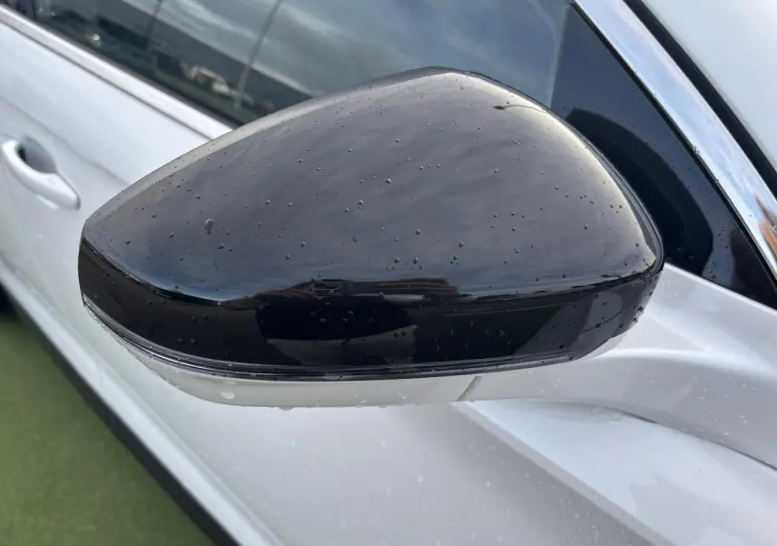 Rétroviseur noir brillant côté gauche du DS7 Crossback blanc nacré avec gouttes d'eau visibles sur la carrosserie.