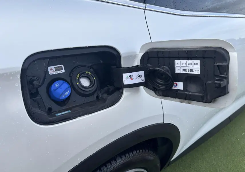 Trappe à carburant ouverte côté gauche du DS7 Crossback blanc nacré, montrant les bouchons diesel et AdBlue.