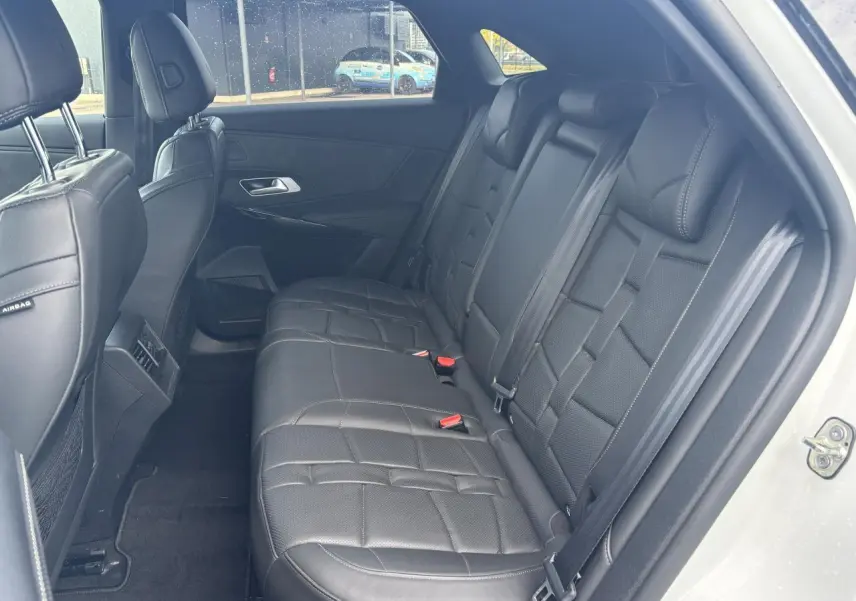 Vue latérale droite de l'habitacle arrière du DS7 Crossback blanc, avec sièges en cuir noir et ceintures visibles.