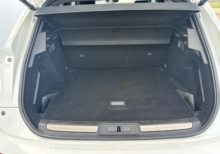 Coffre ouvert vu de l'arrière d'un DS7 Crossback blanc, avec tapis noir et cache-bagages déployé.