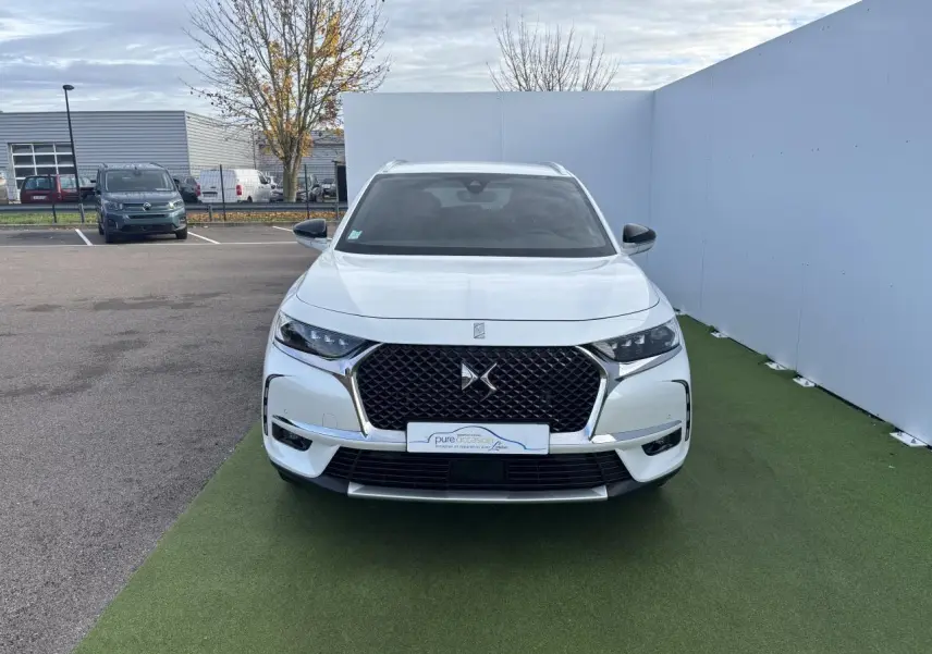Vue frontale d'un DS7 Crossback blanc nacré avec calandre DS Wings chromée et phares LED distinctifs.