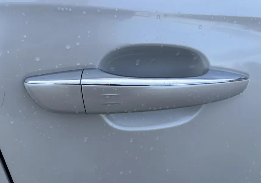 Poignée de porte chromée sur la portière blanche côté gauche du DS7 Crossback 2021, avec gouttes d'eau visibles.