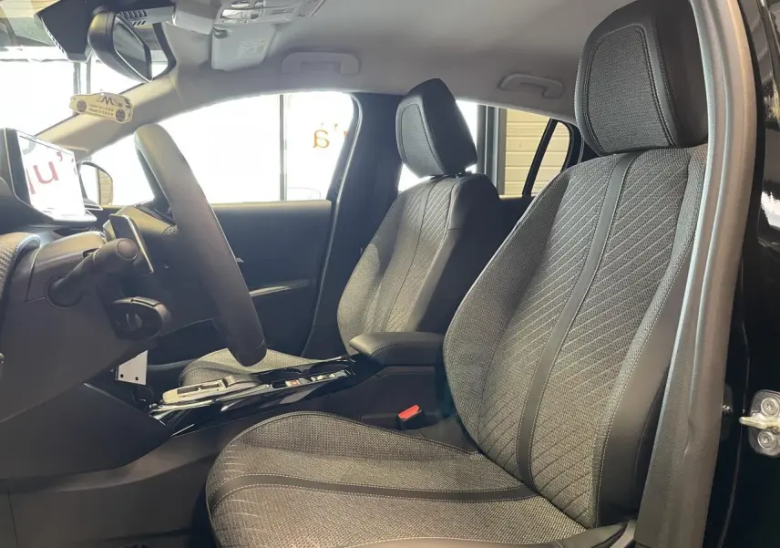 Vue intérieure côté conducteur de la Peugeot 208 noire, mettant en valeur les sièges tissu gris et le volant compact cuir.