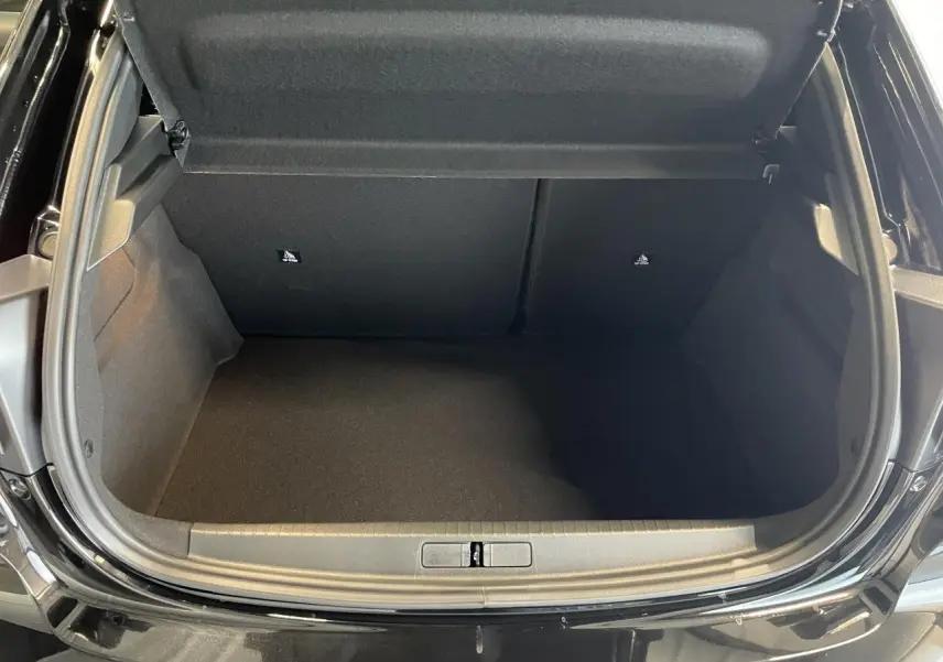 Coffre ouvert vu de l'arrière d'une Peugeot 208 noire, montrant un espace de rangement vide et propre.