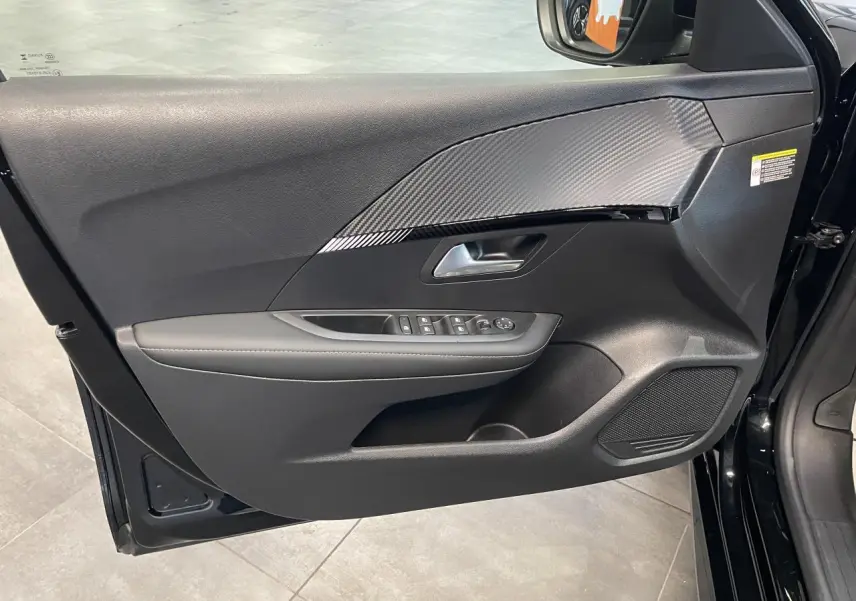 Vue intérieure côté gauche de la porte noire du Peugeot 208 Allure 2025 avec insert effet carbone et commandes électriques.