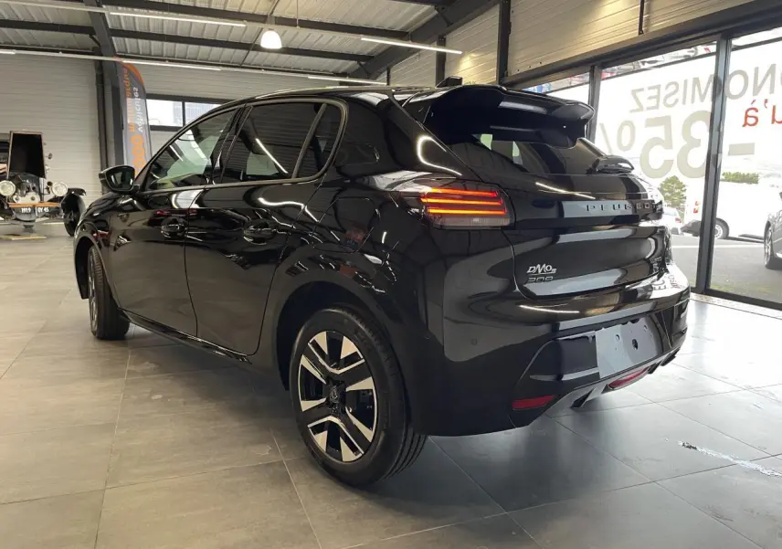 Peugeot 208 noire vue 3/4 arrière droit en intérieur, avec feux arrière allumés et jantes alliage bi-tons.