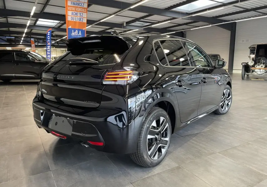 Peugeot 208 hybride noire vue 3/4 arrière droit en intérieur avec jantes alliage bi-tons et feux LED.