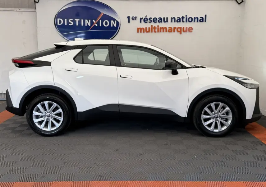 Profil côté gauche du Toyota C-HR blanc 2024, version 1.8 Hybride 140 Dynamic, sur fond intérieur showroom.