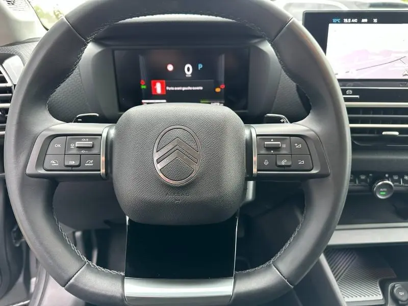 Vue rapprochée du volant cuir noir du Citroën C4 X 2025 avec commandes intégrées et tableau de bord numérique en arrière-plan.