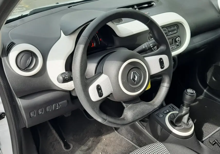 Vue intérieure côté conducteur de la Renault Twingo III blanc cristal, volant multifonction et levier de vitesse manuel visibles.