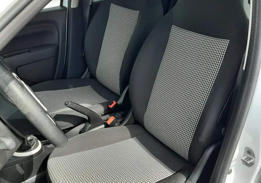 Vue intérieure côté gauche des sièges avant en tissu gris noir de la Renault Twingo III blanc cristal, avec volant et frein à main visibles.
