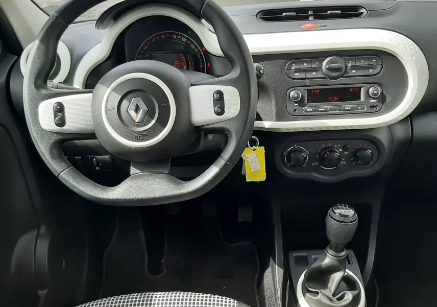 Vue intérieure du tableau de bord et volant de la Renault Twingo III blanche, avec levier de vitesse manuel et commandes centrales visibles.