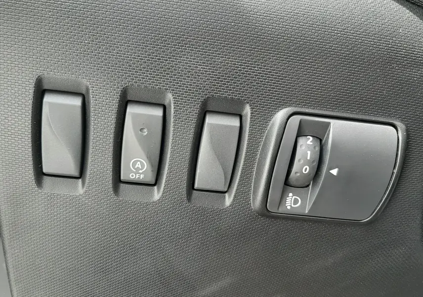 Panneau de commandes intérieures noires avec interrupteurs et molette de réglage des phares dans une Renault Twingo III blanc cristal.
