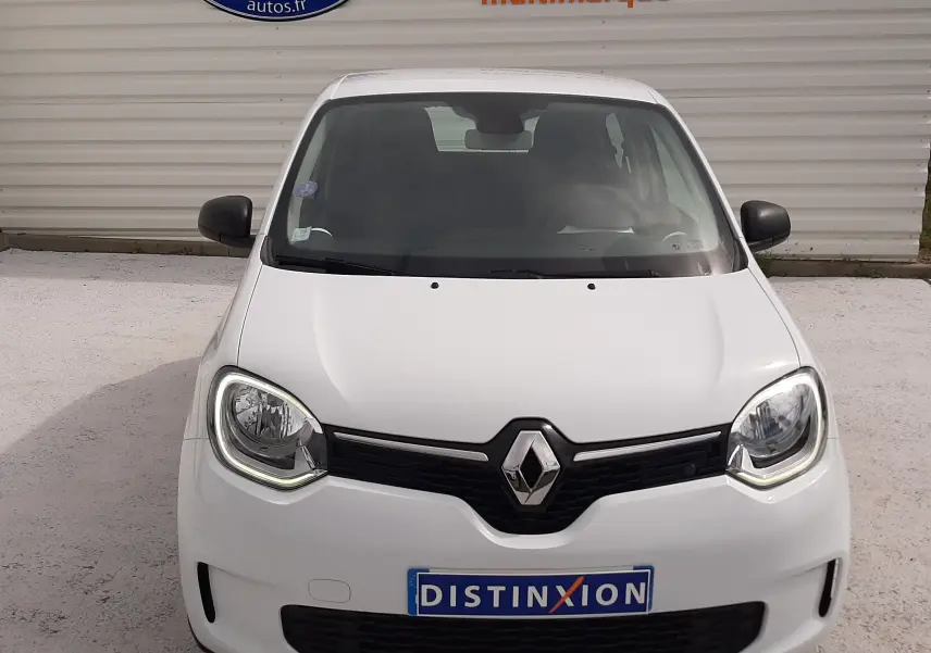 Vue de face d'une Renault Twingo III blanc cristal avec calandre noire et phares allumés sur fond clair.