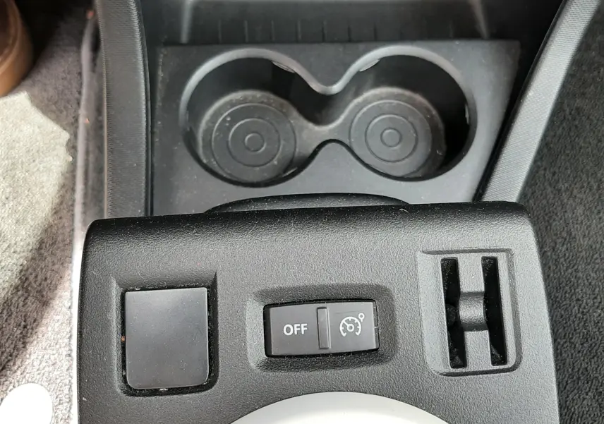 Vue rapprochée du tableau de commande noir avec bouton de régulateur de vitesse et porte-gobelets dans une Renault Twingo III blanc cristal.