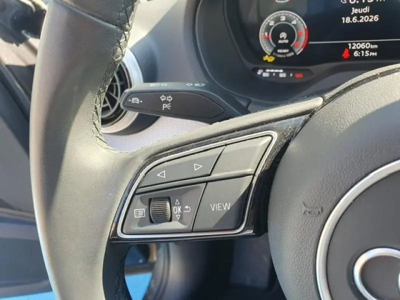 Gros plan sur les commandes gauche du volant cuir d’un Audi Q2 gris Manhattan, avec affichage digital en arrière-plan.
