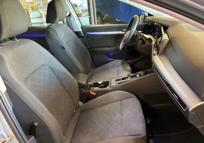 Vue intérieure côté conducteur de la Volkswagen Golf 1.0 eTSI 110 DSG7 Life Plus 2023 avec sièges tissu gris et éclairage d'ambiance violet.