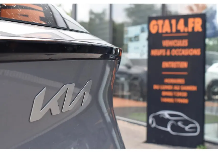 Gros plan sur l'arrière gris du KIA Sportage 2026 avec logo KIA et reflet de vitrine en arrière-plan.