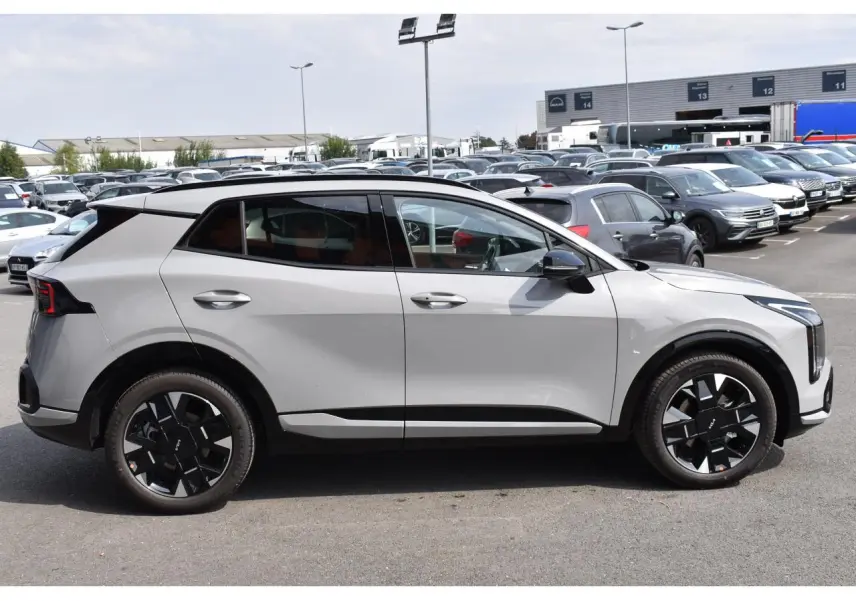 Vue de profil côté gauche du KIA SPORTAGE hybride gris 2026 avec jantes noires distinctives et vitres surteintées.