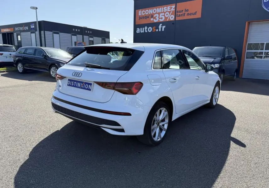 Audi A3 Sportback blanc Arcona vue 3/4 arrière droit sur parking avec jantes alliage 17 pouces et feux arrière LED.