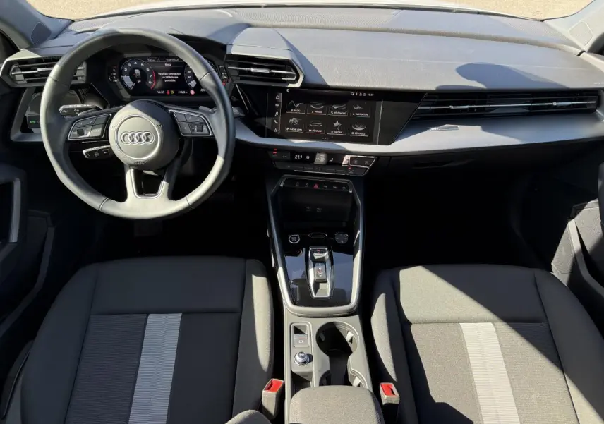Vue intérieure avant de l'Audi A3 Sportback 2024 avec tableau de bord noir et volant cuir multifonctions.