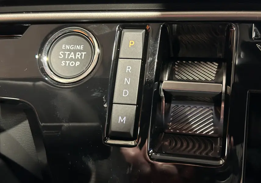 Gros plan sur la console centrale noire brillante du Peugeot 3008 Hybrid avec bouton start/stop et sélecteur de boîte automatique.