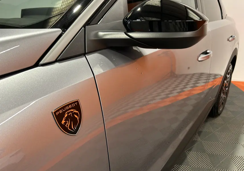 Vue côté gauche rapprochée du Peugeot 3008 gris Artense avec logo lion noir et orange sur l'aile avant.
