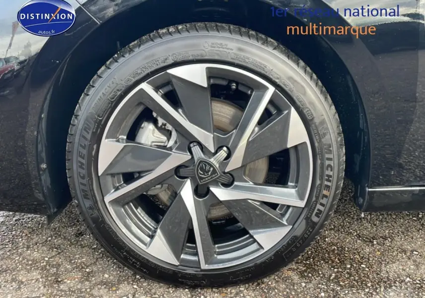 Gros plan sur la roue avant droite noire d'une Peugeot 308 1.2 hybrid 145 allure e-dcs6 avec jante alu bicolore.