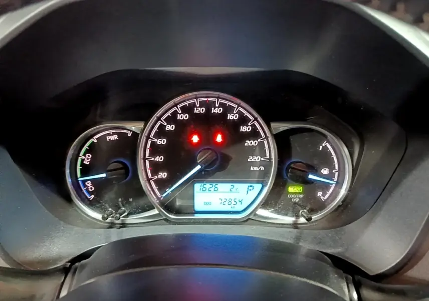 Vue rapprochée du tableau de bord de la Toyota Yaris hybride blanche, affichant la vitesse, jauge et indicateurs lumineux.