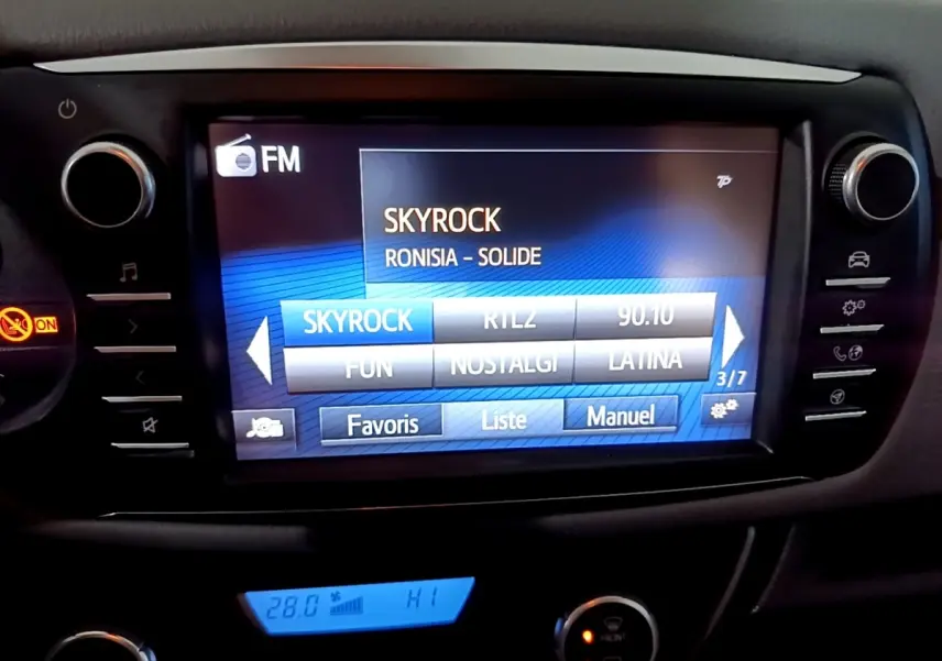 Écran tactile central de la Toyota Yaris blanche 2020 affichant la radio FM sur Skyrock, avec commandes autour.