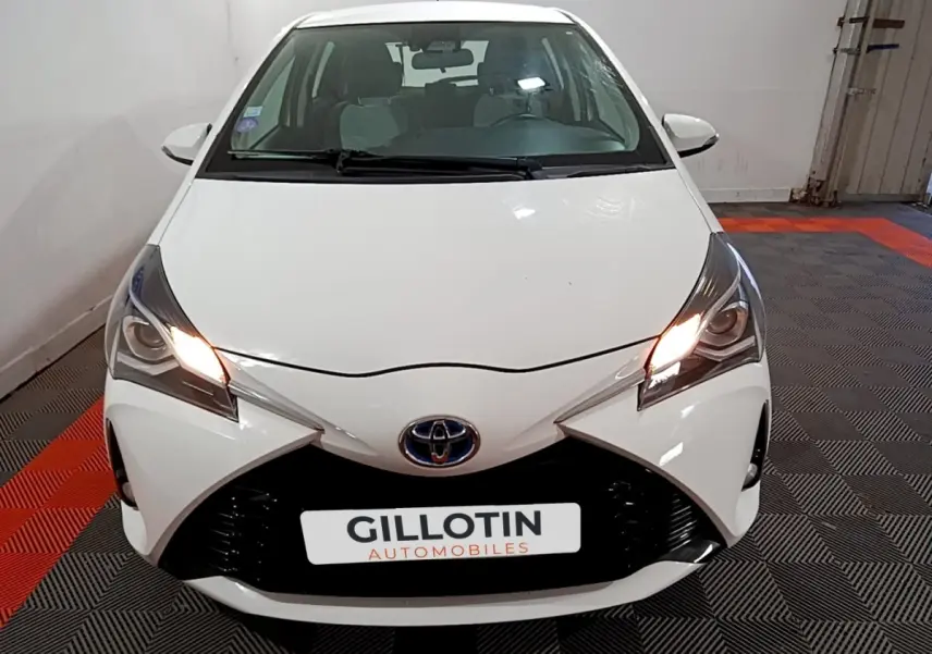 Vue avant d'une Toyota Yaris blanche 2020 avec feux allumés, calandre noire et logo Toyota visible.