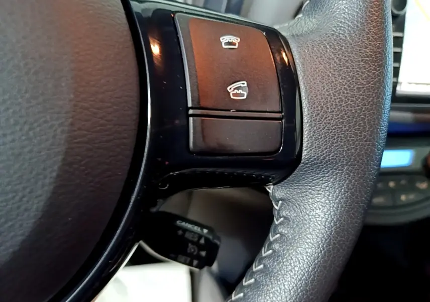 Gros plan sur les commandes noires du volant cuir et alu de la Toyota Yaris blanche, version hybride 2020.