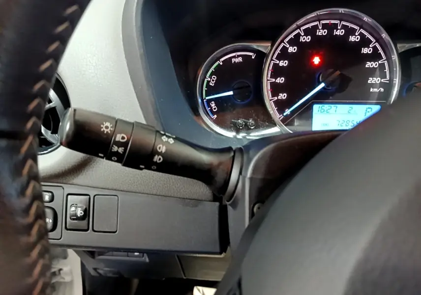 Gros plan sur le tableau de bord et le volant cuir noir de la Toyota Yaris hybride, avec compteurs éclairés et commandes lumineuses.