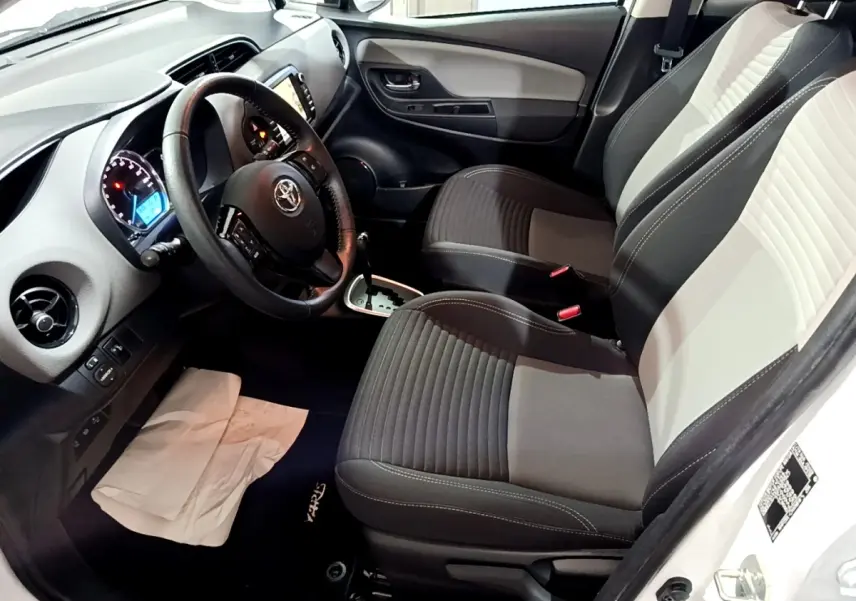 Intérieur avant droit de Toyota Yaris blanche, volant multifonctions cuir, sièges bi-ton gris clair et foncé.