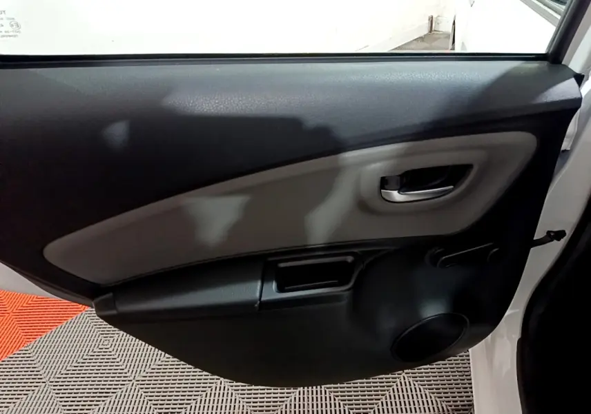 Vue intérieure de la porte arrière droite d'une Toyota Yaris blanche, avec poignée chromée et manivelle de vitre.