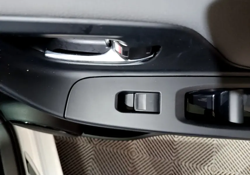 Poignée de porte intérieure chromée et commandes de lève-vitre sur la portière avant gauche d'une Toyota Yaris blanche.