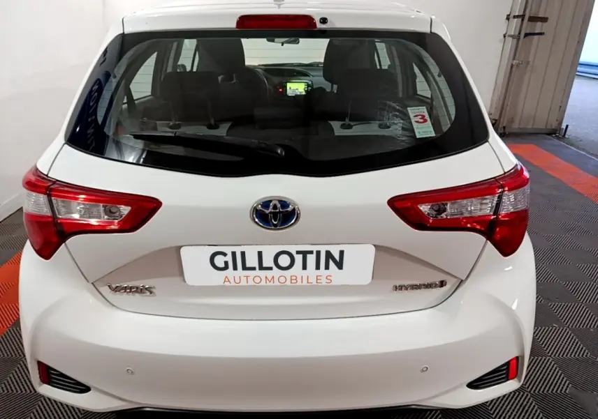 Vue arrière d'une Toyota Yaris blanche 1.5 Hybride 2020 avec feux distinctifs et logo Toyota visible.