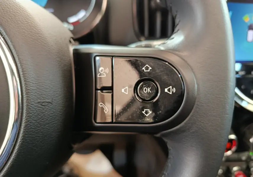 Gros plan sur les commandes multifonctions noires du volant cuir d'un MINI Countryman gris foncé, intérieur moderne.