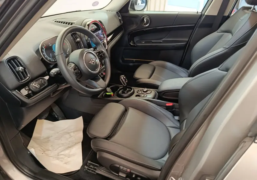 Intérieur avant droit du MINI Countryman gris foncé 2023, avec sièges cuir noirs et tableau de bord digital lumineux.