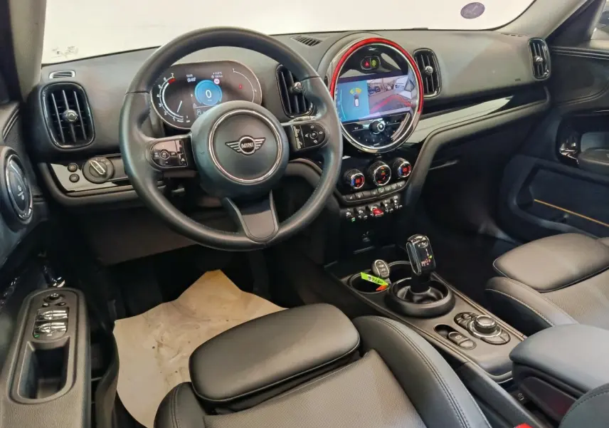 Vue intérieure avant droite du MINI Countryman 2023, tableau de bord noir avec écran tactile rond et volant cuir noir.
