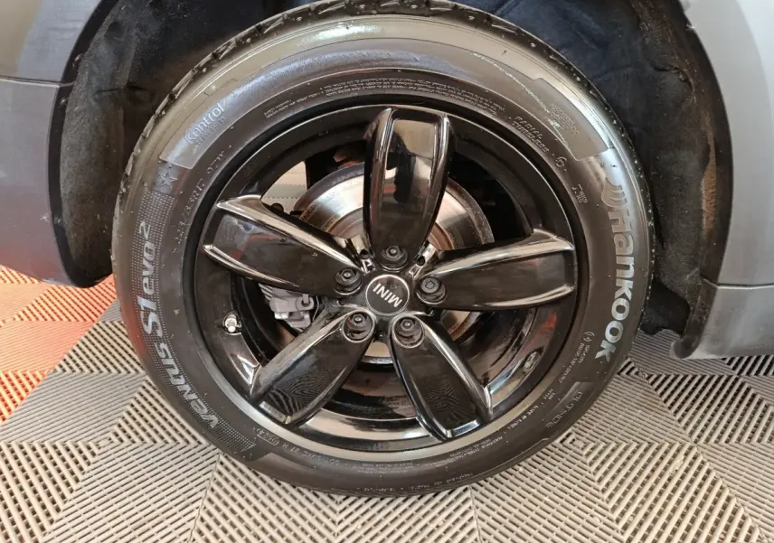 Gros plan sur la roue avant droite noire brillante du MINI Countryman gris foncé, avec jante cinq branches et logo MINI.