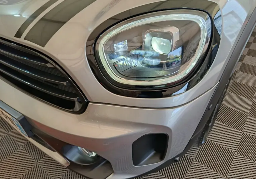 Gros plan sur le phare avant droit et la calandre d’un MINI Countryman gris foncé, détails noirs contrastants visibles.