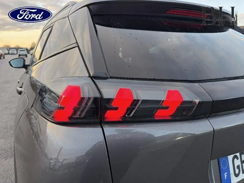 Gros plan sur le feu arrière droit rouge du Peugeot 2008 gris Artense, avec lunette arrière teintée et becquet visible.