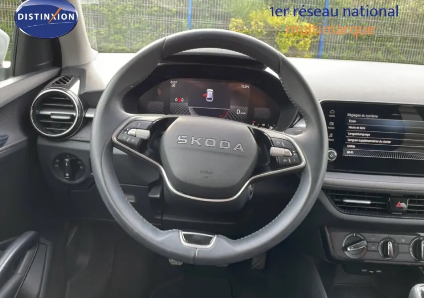 Vue intérieure centrée sur le volant SKODA avec tableau de bord numérique et écran tactile du système multimédia.