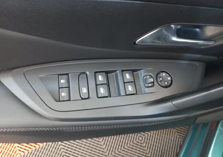 Gros plan sur les commandes de lève-vitres et rétroviseurs sur la porte côté gauche d’une Peugeot 308 bleu.